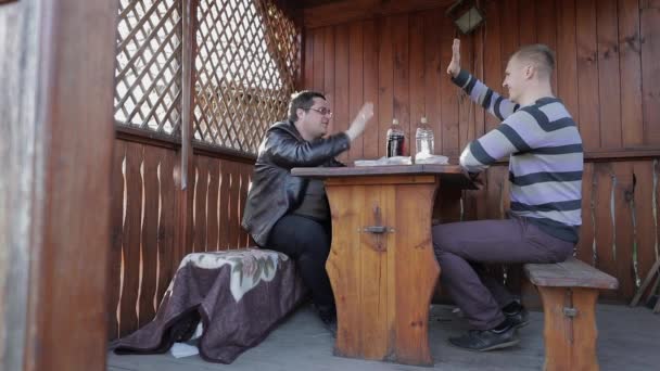 Two men sit at the table and drink beer from plastic bottles. Happy — Stock Video