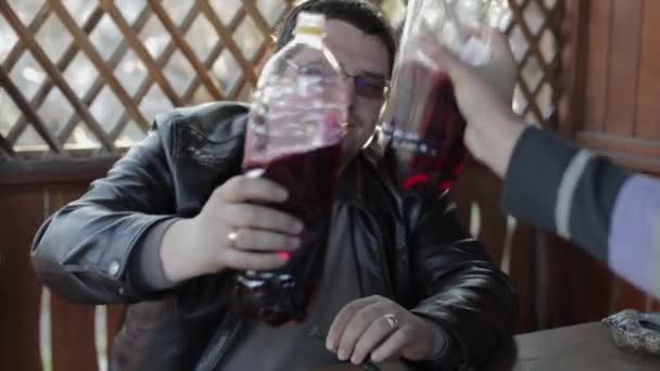 Twee mannen zitten aan de tafel en drinken bier uit plastic flessen. Gelukkig — Stockvideo