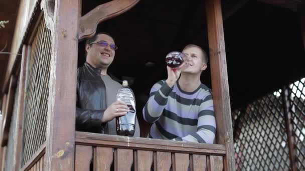Двое мужчин на террасе пьют пиво из пластиковых бутылок и говорят: — стоковое видео
