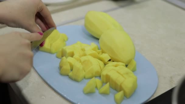 Женщина режет картошку на голубой доске — стоковое видео