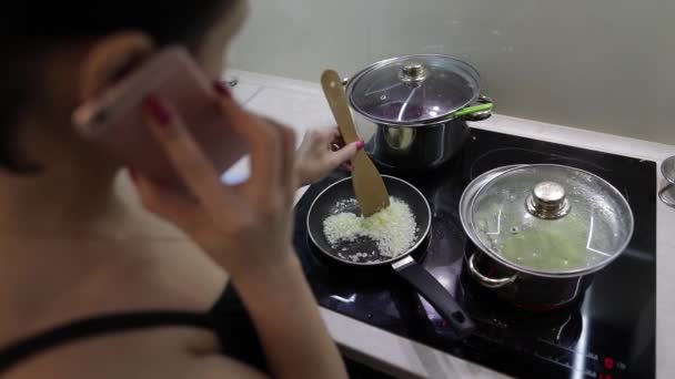 Hermosa mujer caucásica hablando por teléfono mientras cocina — Vídeos de Stock