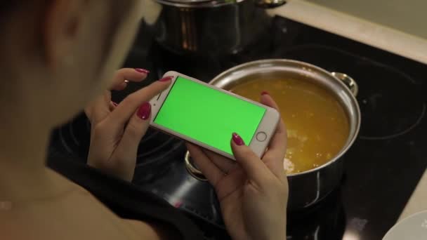 Mujer está sosteniendo un teléfono inteligente con una pantalla verde, y cocinar sopa — Vídeo de stock