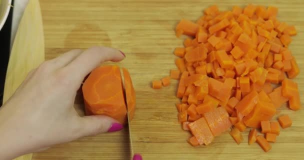 Женщина-домохозяйка разрезает морковь на кусочки на кухне — стоковое видео
