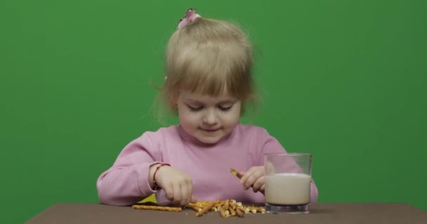 A criança come bolachas. Uma menina está comendo biscoitos sentados na mesa . — Vídeo de Stock