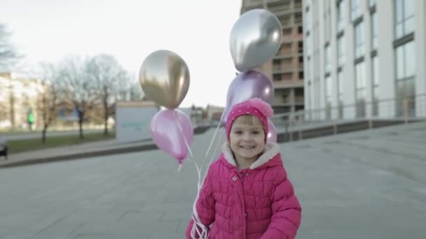 Šťastné dítě běží po ulici s balónky s heliem — Stock video