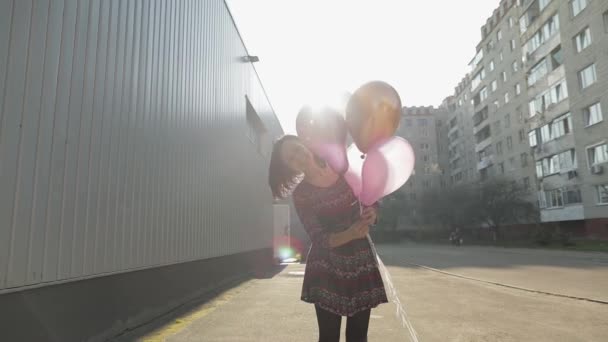 Jolie femme en robe tenant des ballons avec de l'hélium à l'extérieur à la lumière du jour — Video