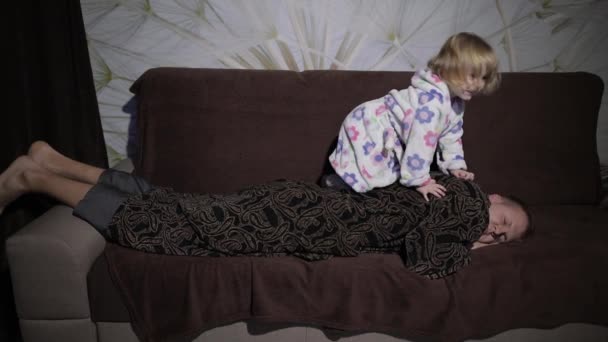 Little girl in bathrobe waking her father up. Man sleeps on the couch — Stock Video