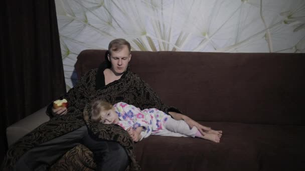 Small daughter with her father watching interesting film and eating apple — Stock Video