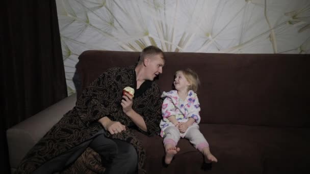 Kis lánya apja néz érdekes film és étkezési Alma — Stock videók