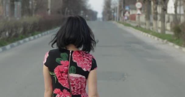 Attrayant jeune femme dans une robe avec des fleurs se tourne vers la caméra et sourit — Video