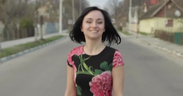 Atractiva mujer joven en un vestido con flores moviéndose a la cámara y sonrisas — Vídeo de stock