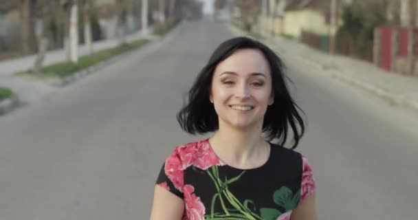 Jovem atraente em um vestido com flores movendo-se para a câmera e sorri — Vídeo de Stock