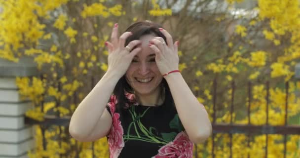 Aantrekkelijke jonge vrouw in een jurk met bloemen maken grappige gezichten — Stockvideo