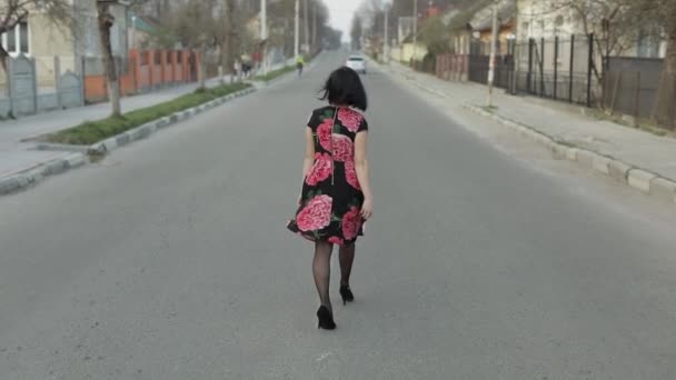 Attractive young woman in a dress with flowers walking on the highway — Stockvideo