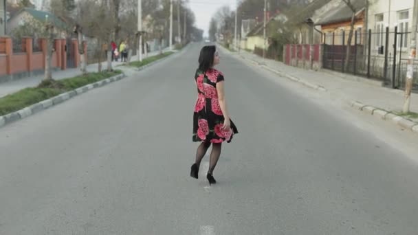 Attractive young woman in a dress with flowers walking on the highway — Stockvideo