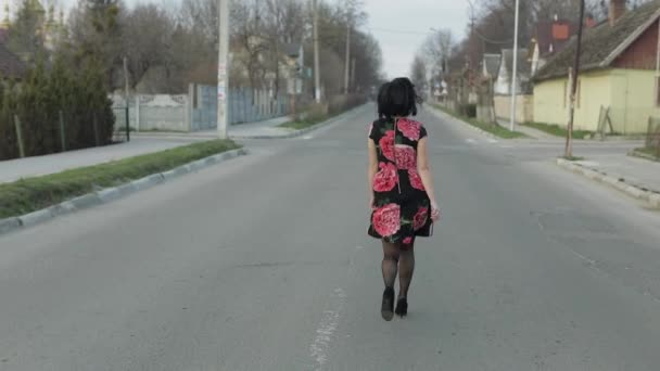 Attractive young woman in a dress with flowers running on the highway — Stockvideo