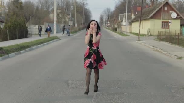 Attractive young woman in a dress with flowers walking on the highway — Stockvideo