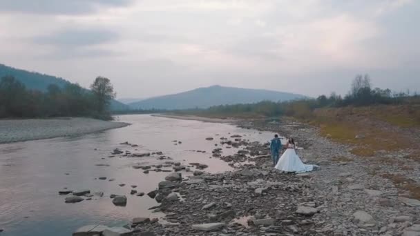 Ślub para stanąć w pobliżu górskiej rzeki. Pan młody i Panna młoda. Widok Arial — Wideo stockowe