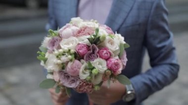 Sokakta elinde düğün buketi ile damat. Pembe gömlek, mavi ceket