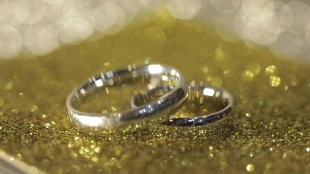 Anillos de plata de la boda acostado en la superficie brillante brillante. Brillando con luz. Primer plano — Vídeos de Stock