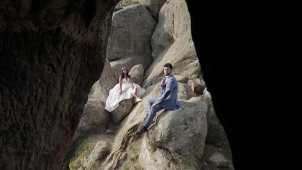 Γαμπρός με τη νύφη κάθονται σε μια υψηλή πλαγιά του βουνού. Ζευγάρι γάμων. Ευτυχισμένο — Αρχείο Βίντεο