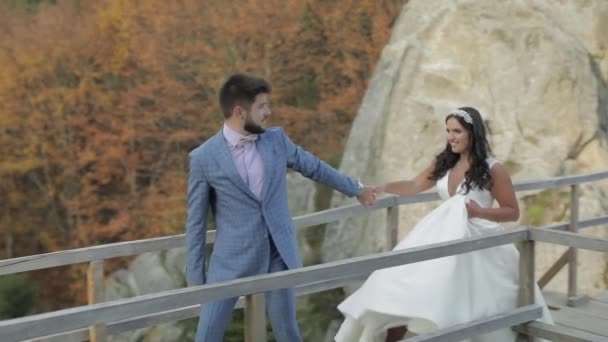 Novio con novia en una bringe cerca de las colinas de montaña en el bosque. Pareja de boda — Vídeo de stock