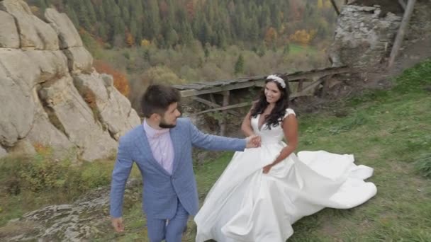 Наречений ходить з нареченою на гірських пагорбах у лісі. Весільна пара — стокове відео