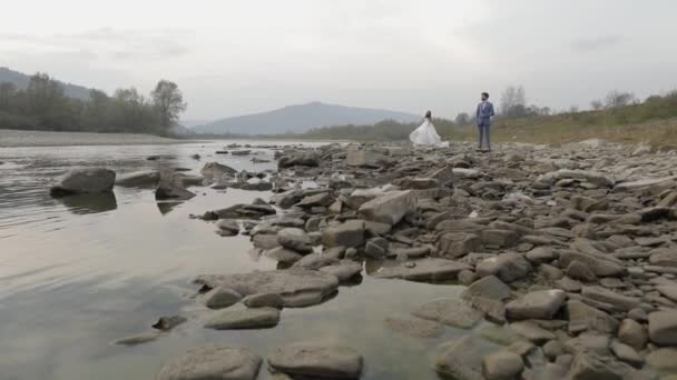 Matrimonio coppia in piedi vicino al fiume di montagna. Sposo e sposa innamorati — Video Stock