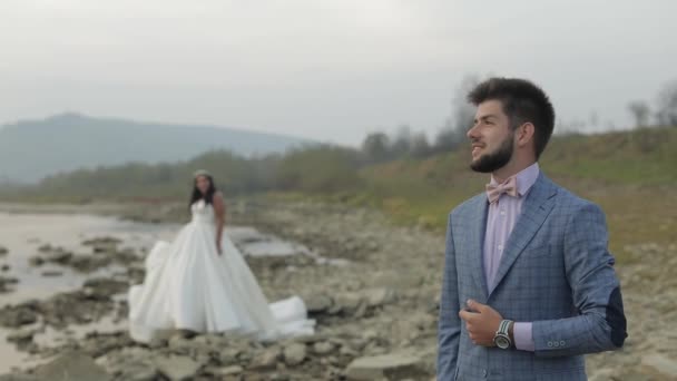 Весільна пара стоїть біля гірської річки. Наречений і наречена закохані — стокове відео