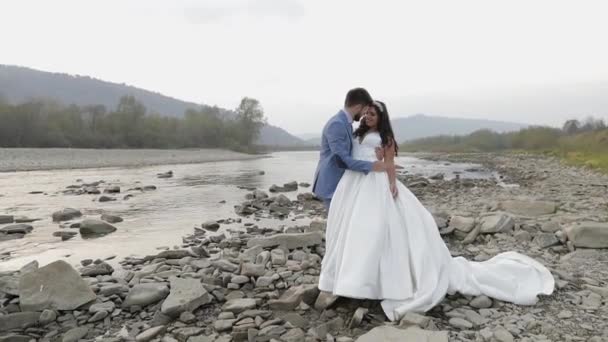 Svatební pár stojí nedaleko horské řeky. Zamilovaný ženich a nevěsta — Stock video