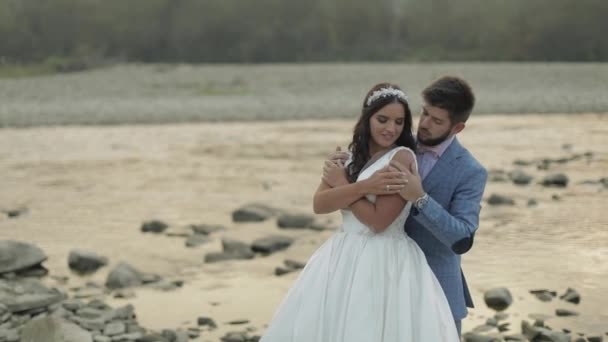 Весільна пара стоїть біля гірської річки. Наречений і наречена закохані — стокове відео