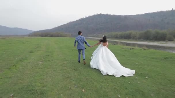 Весільна пара біжить поблизу гірської річки. Наречений і наречена закохані — стокове відео