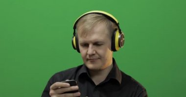 Adam kablosuz sarı kulaklıkla müzik dinliyor ve dans ediyor. Yeşil Ekran