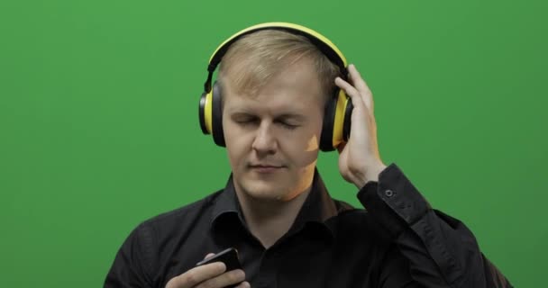 Guy listens to music in wireless yellow headphones and dances. Green screen — Stock Video