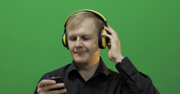 Facet słucha muzyki w bezprzewodowych żółtych słuchawkach i tańcach. Zielony ekran — Wideo stockowe