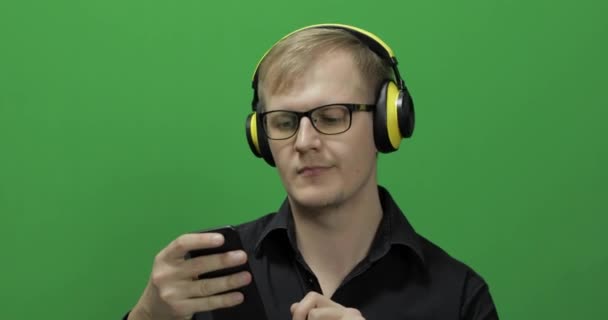A fickó zenét hallgat vezeték nélküli sárga fejhallgatóban és táncban. Zöld képernyő — Stock videók
