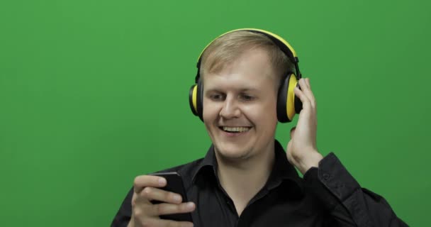 El tipo escucha música en auriculares y bailes inalámbricos amarillos. Pantalla verde — Vídeo de stock