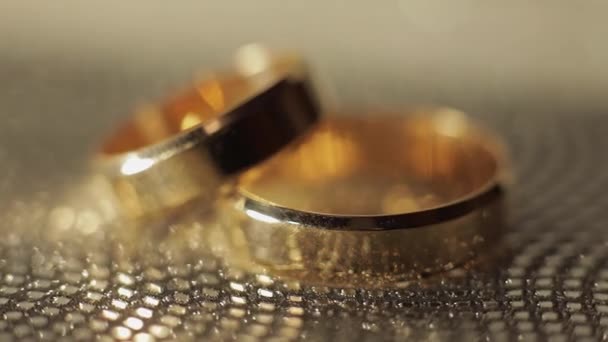 Bröllop Gols ringar liggande på glänsande glänsande yta. Lyser med ljus. Närbild — Stockvideo