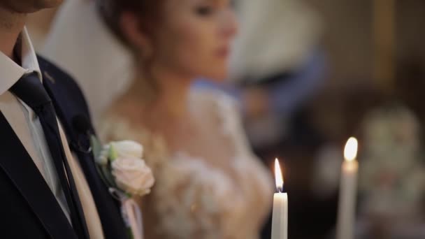 De bruid en de bruidegom staan in de kerk, houden kaarsen in hun handen — Stockvideo