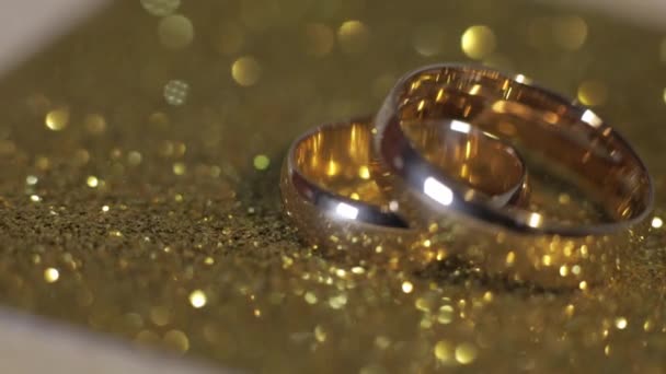 Весільні золоті кільця лежать на блискучій глянцевій поверхні. Сяє зі світлом. Крупним планом — стокове відео
