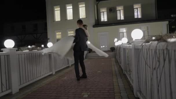 Bruidegom met bruid in koude avond op een brug bedekt met vele lantaarns. Herfst — Stockvideo