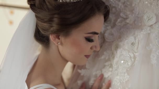 Όμορφη και υπέροχη νύφη σε νυχτερινό φόρεμα στέκεται κοντά στο νυφικό. Γάμου — Αρχείο Βίντεο