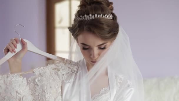 Beautiful and lovely bride in night gown stands near wedding dress. Wedding — Stock Video