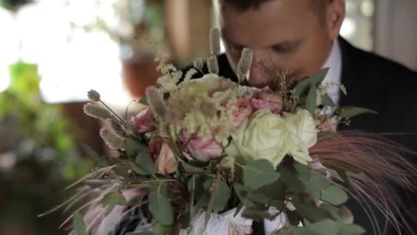 Schöner Bräutigam steht am Fenster mit einem Strauß Hochzeitsblumen — Stockvideo