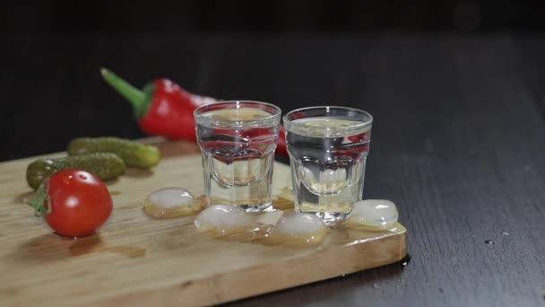 Vodka en vasos de chupito sobre tabla de madera rústica. Añadir cubitos de hielo . — Vídeos de Stock