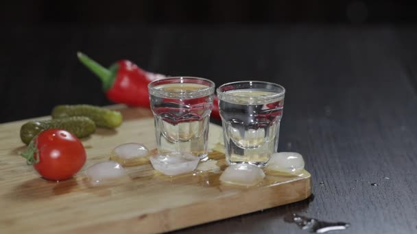 Wodka im Schnapsglas auf rustikalem Holzbrett. Eiswürfel hinzufügen. — Stockvideo