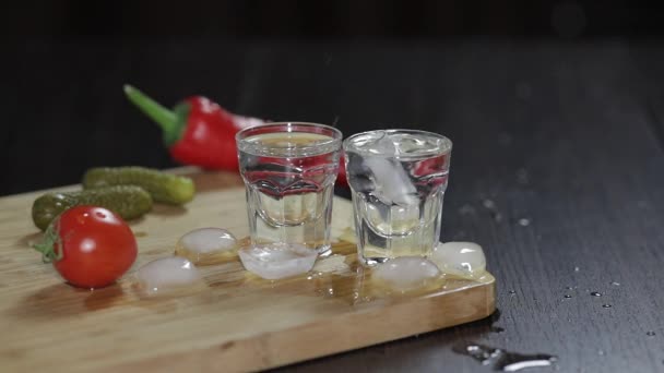 Wodka in shot glazen op rustieke houten bord. Ijsblokjes toevoegen. — Stockvideo