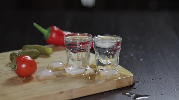Wodka in shot glazen op rustieke houten bord. Ijsblokjes toevoegen. — Stockvideo
