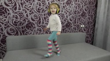 Küçük mutlu çocuk atlama ve kanepede dans ve kulaklık müzik dinleme