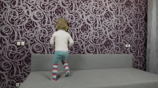 Μικρό ευτυχισμένο παιδί άλμα και χορό στον καναπέ και ακούγοντας μουσική στα ακουστικά — Αρχείο Βίντεο